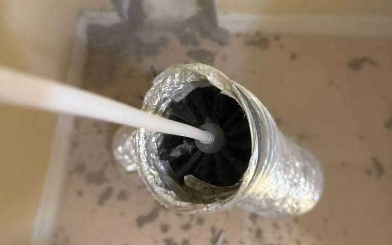 A rotary brush on a white cable pushed through a foil flex duct coated with lint