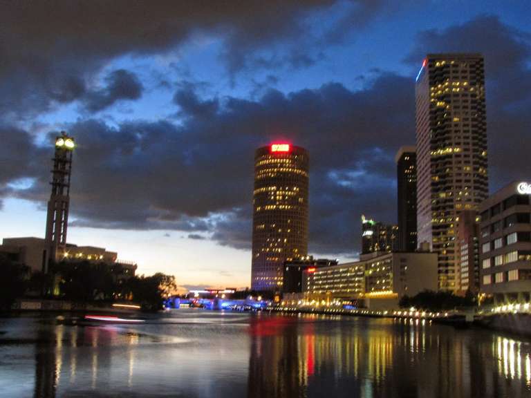 The Tampa Riverwalk at dusk, downtown towers lit up and reflected in the Hillsborough River